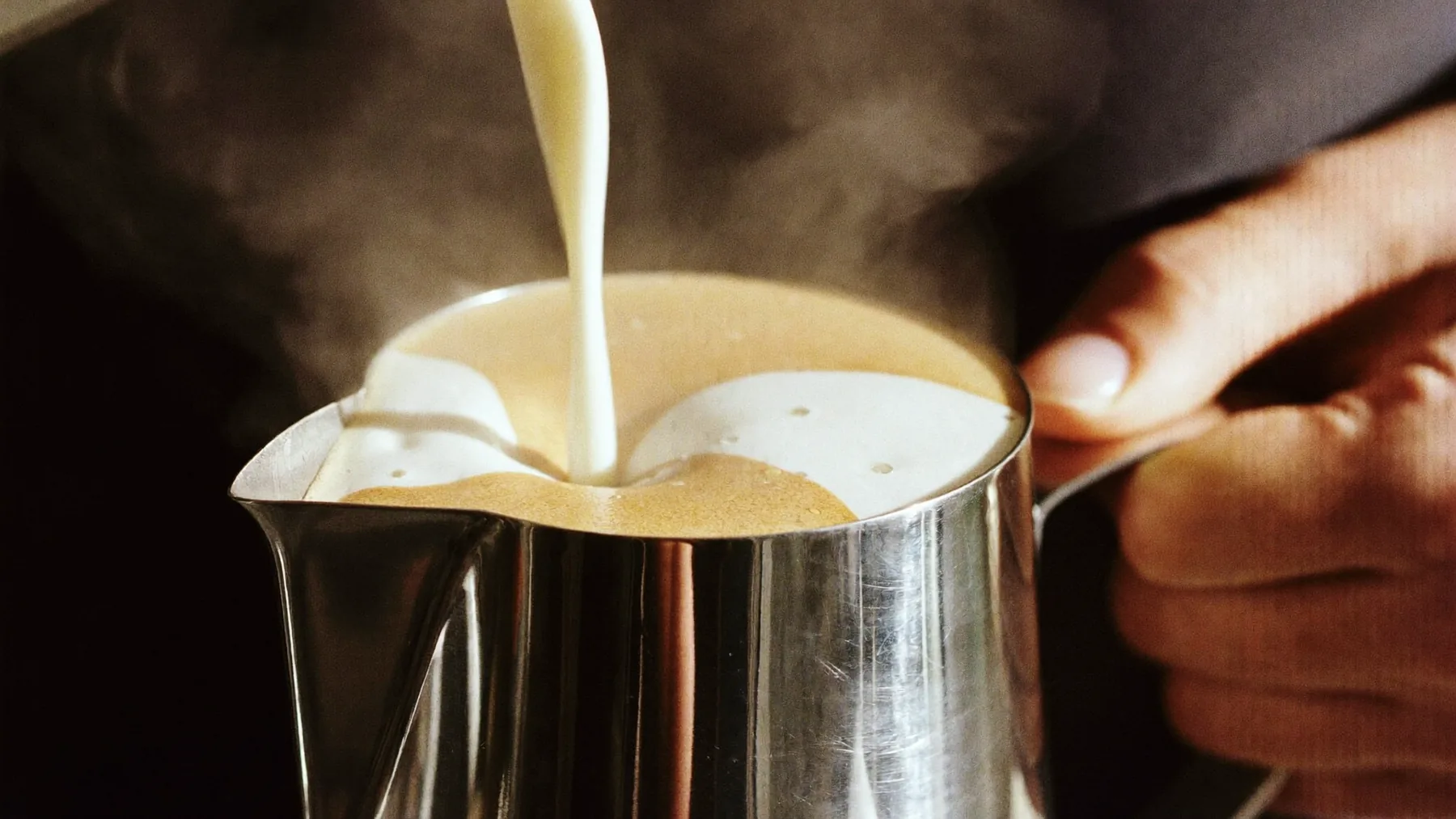 Milk being poured into a stainless steel pitcher